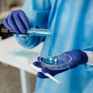 medical researcher pouring blue liquid into a petri dish
