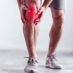 man in running shorts and shoes holding his knee, which is highlighted in red, in pain